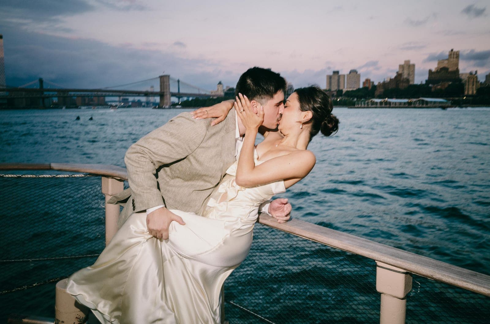 Andie & Jake kissing aboard the ship with the Brooklyn Bridge behind them